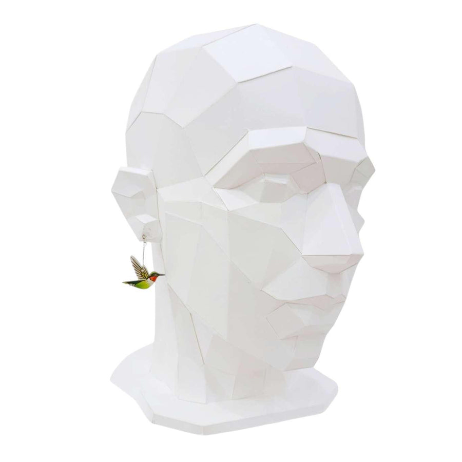 Geometric white mask on a mannequin head with a small bird figurine.