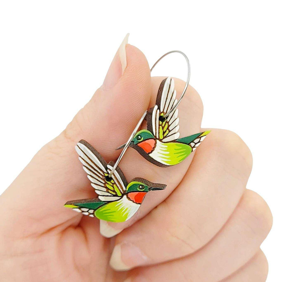 Hand holding a pair of hummingbird earrings with a white background