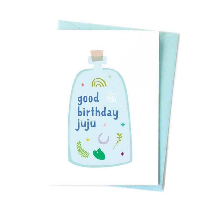 A birthday blank-inside card with a hand-illustrated image of a blue bottle with leaves and stars with the words good birthday juju written on the front